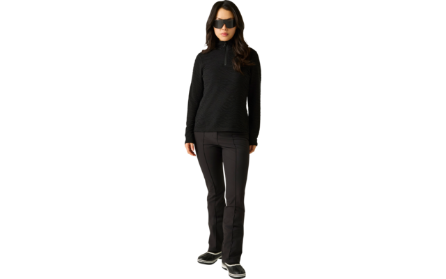 Person steht frontal, trägt schwarze Sonnenbrille, schwarzen Reißverschluss-Pullover mit langen Ärmeln, schwarze Hose und schwarze Schuhe vor hellem Hintergrund