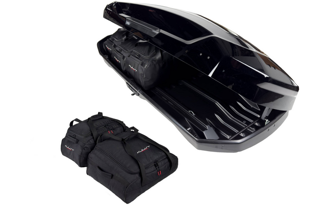 Coffre de toit noir ouvert, avec un sac de voyage noir à l'intérieur et trois sacs noirs à côté