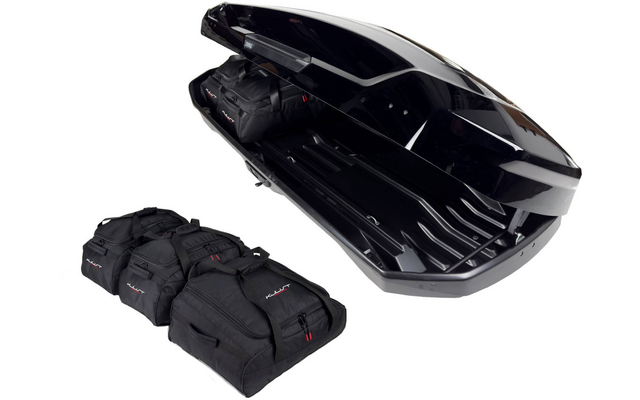 Coffre de toit noir ouvert sur fond blanc à côté de quatre sacs de voyage noirs