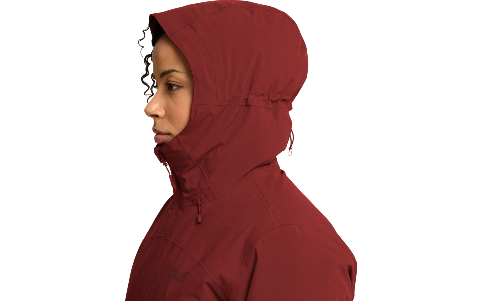 Persona de perfil mirando a la izquierda, rostro visible, lleva una chaqueta con capucha rojo oscuro, capucha levantada y cremallera cerrada