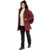 Persona con abrigo rojo, sudadera con capucha blanca, pantalones negros y botas de senderismo, lleva una mochila negra y camina