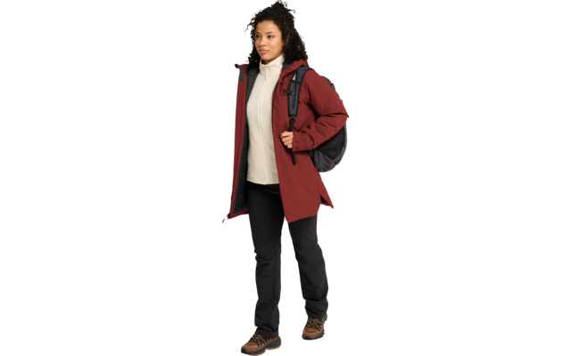 Persona con abrigo rojo, sudadera con capucha blanca, pantalones negros y botas de senderismo, lleva una mochila negra y camina
