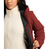Vista parcial de una persona que sostiene abierta una chaqueta roja, mostrando un forro polar crema con cierre y pequeño logo blanco; visibles mentón, cuello, torso superior y mano