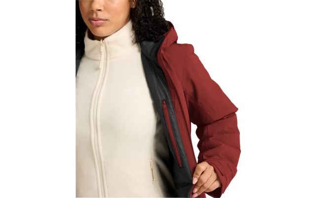 Vista parcial de una persona que sostiene abierta una chaqueta roja, mostrando un forro polar crema con cierre y pequeño logo blanco; visibles mentón, cuello, torso superior y mano
