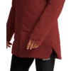 Vista parcial de una persona con chaqueta acolchada rojo oscuro con cremallera y abertura lateral, mano visible, mallas negras con logotipo blanco 'Wolfskin'