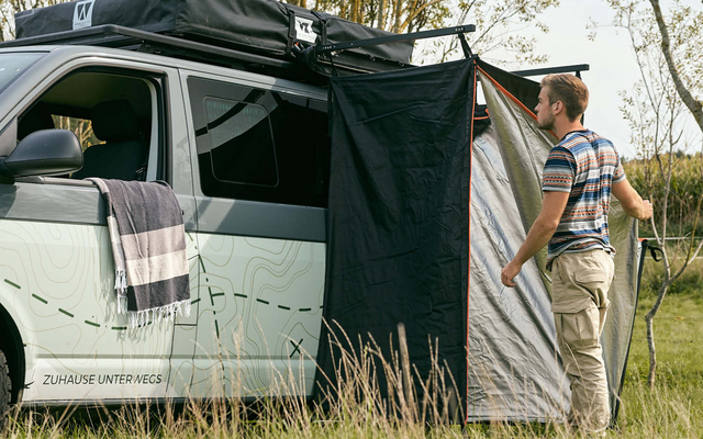 Una autocaravana con un toldo adjunto, dos personas de pie al lado en un campo de hierba