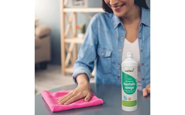 Person wischt einen Tisch mit einem rosa Tuch; Flasche Haushaltsreiniger steht daneben