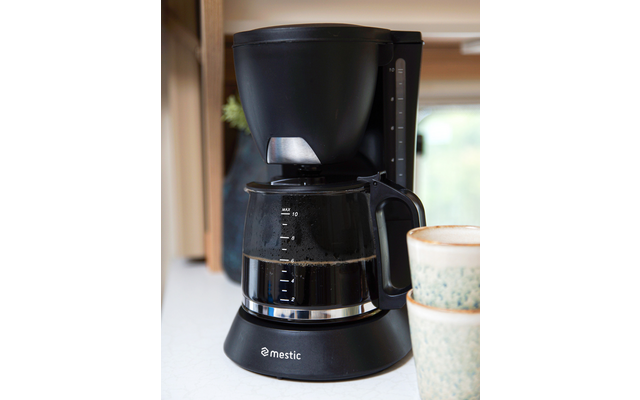 Black coffee maker with glass carafe on a countertop next to two cups