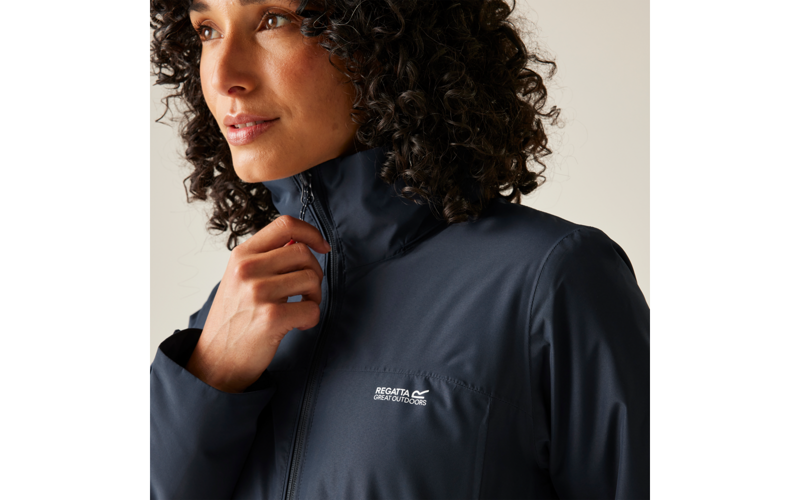 Femme aux cheveux bouclés portant une veste bleu foncé et tenant le col avec la main