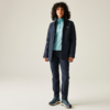 Homme aux cheveux bouclés portant un jean bleu, un pull bleu clair et un manteau sombre, debout devant un fond clair