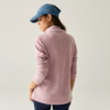 Persona vista da dietro che indossa una giacca in pile rosa, un berretto blu e pantaloni scuri su uno sfondo chiaro uniforme