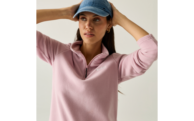 Persona con un berretto da baseball blu e un maglione rosa, mani sul berretto