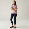 Persona in piedi con le braccia incrociate, indossa un maglione rosa con mezza zip, leggings blu scuro, calzini rosa e sneaker bordeaux su sfondo chiaro e uniforme