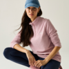 Persona seduta con un ginocchio sollevato su sfondo chiaro, indossa una felpa rosa con zip corta, leggings blu scuro, un berretto da baseball blu e lunghi capelli scuri
