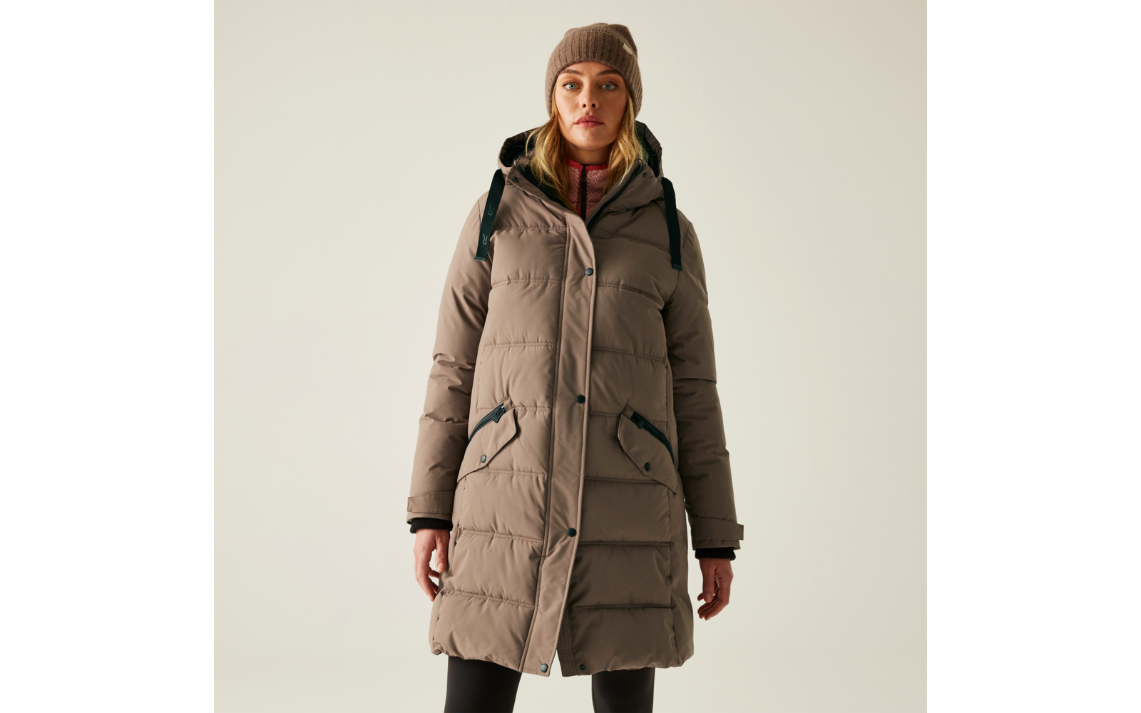 Frau trägt lange beige Winterjacke mit Kapuze und schwarzen Rucksack