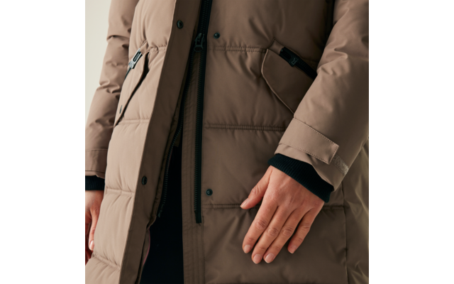 Eine Person trägt eine beige Winterjacke und legt die rechte Hand auf den Körper