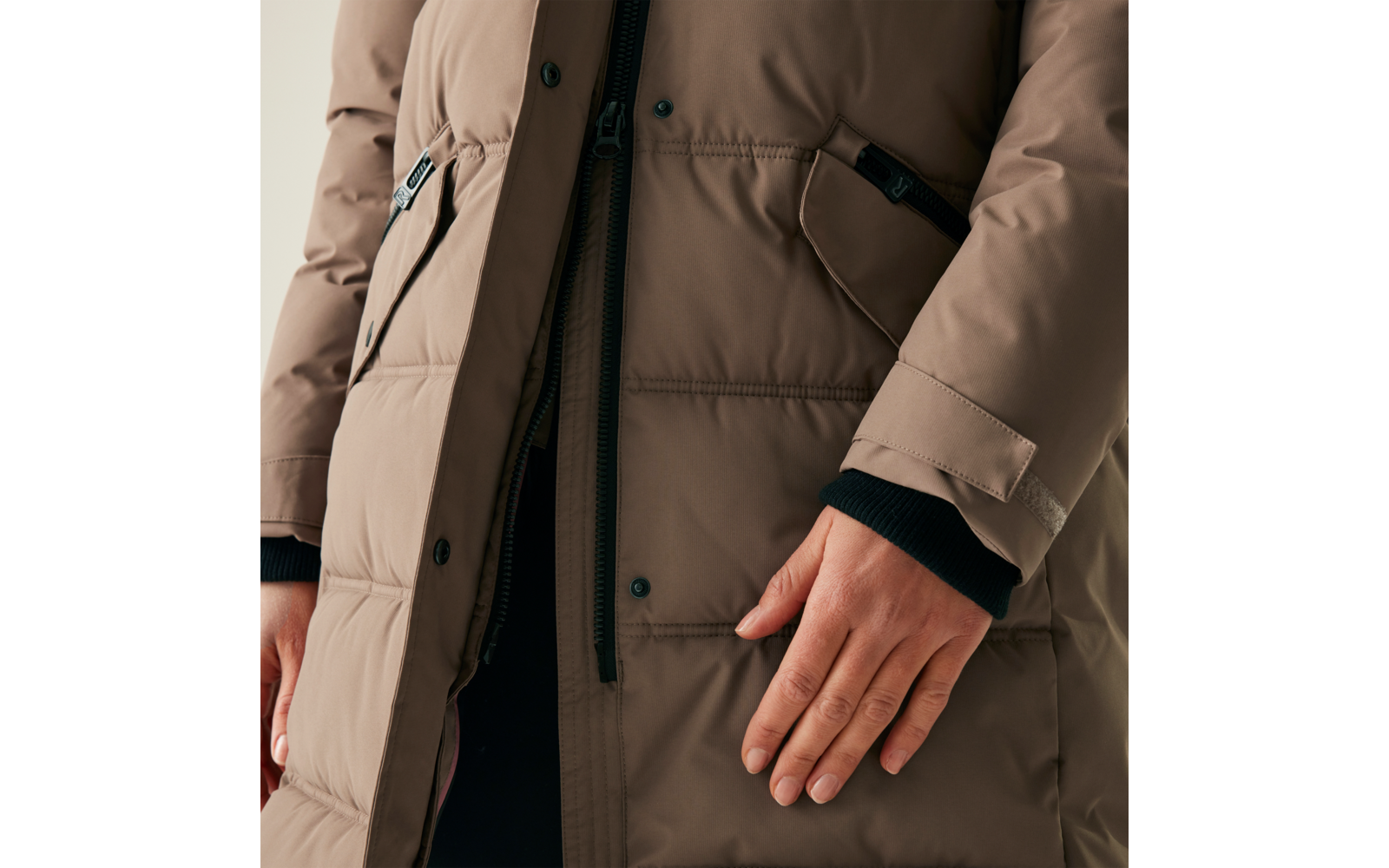 Eine Person trägt eine beige Winterjacke und legt die rechte Hand auf den Körper