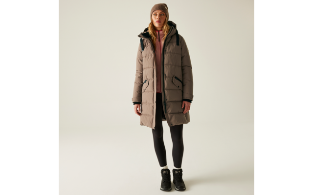 Frau trägt lange winterliche Jacke mit Kapuze, darunter schwarze Hose und Schuhe, vor hellem Hintergrund