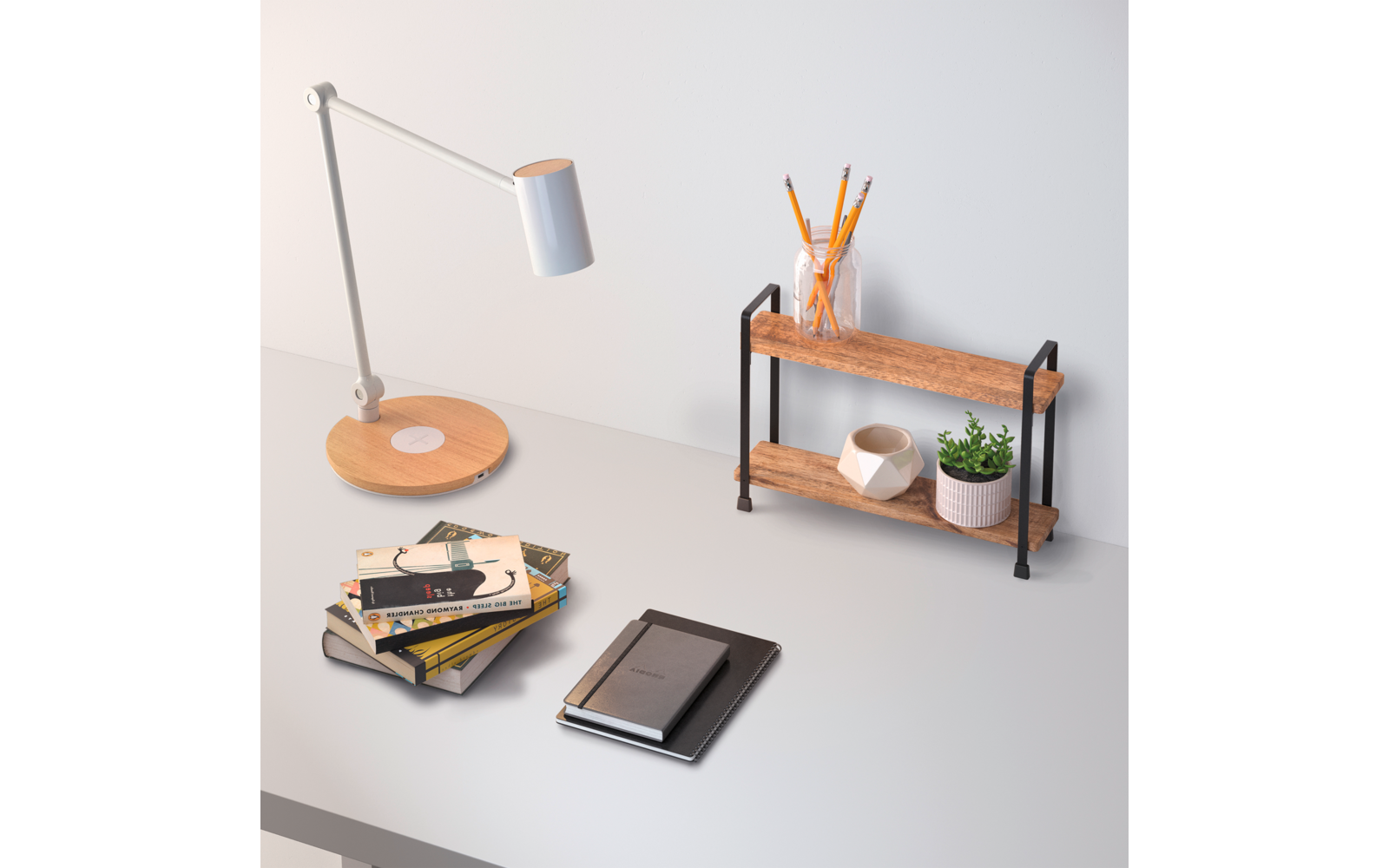 Tischfläche mit weißer Tischlampe, Holzfuß; Stapel Bücher, geschlossenes Notizbuch mit Tablet; kleines zweistöckiges Holzregal mit Glas mit Bleistiften, weißer Keramikschale und kleinem Topf mit grüner Pflanze