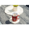 Tasse rouge avec couvercle transparent et anse, logo blanc à l'avant, posée sur un dessous de tasse crocheté blanc sur une table en bois foncé; plante en pot sur un autre dessous en arrière-plan