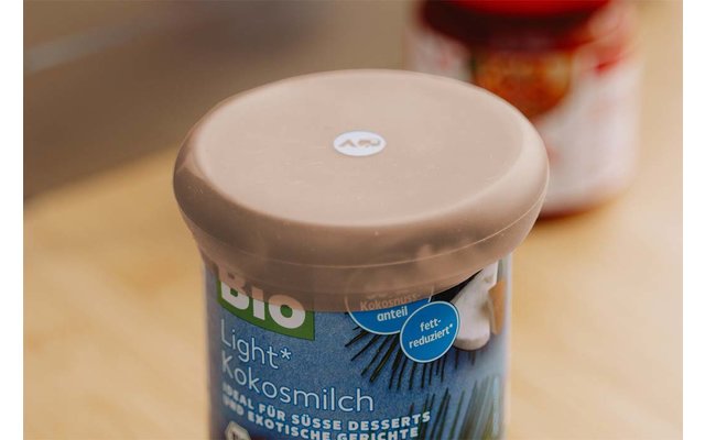 Bekertje met beige kunststofdeksel en blauw etiket met opschrift 'BIO Light Kokosmilch' op een houten ondergrond; op de achtergrond onscherpe pot met rood deksel