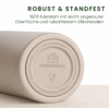 Beige liegender zylindrischer Becher, Nahaufnahme des Bodens mit runder, geprägter Silikonsohle; zentraler Stempel mit Bäumen und Text 'GRØNENBERG', zwei Piktogramme; umlaufender Text 'love your everyday', 'do not microwave', 'hand wash only' und Web