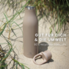 Beige Edelstahl-Trinkflasche steht im Sand zwischen Dünengras, Schraubverschluss liegt daneben; weißer Text: 'GUT FÜR DICH & DIE UMWELT' und '90% recycelter Edelstahl'