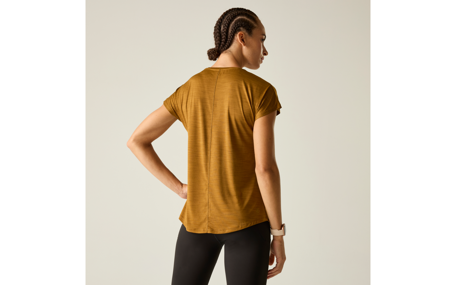 Person von hinten, trägt senfgelbes Kurzarmshirt und schwarze Leggings, geflochtene Haare, Armbanduhr am Handgelenk