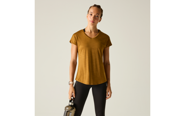 Person steht vor hellem Hintergrund, Haare zurückgebunden, trägt kurzes senffarbenes V‑Ausschnittshirt und schwarze Leggings, hält in der rechten Hand eine Trinkflasche