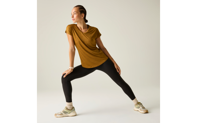 Person mit geflochtenen Haaren in weitem seitlichem Ausfallschritt, trägt mosterdfarbenes Kurzarmshirt, schwarze Leggings, weiße Socken und beige Sportschuhe, schaut nach links vor hellem Hintergrund