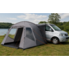 Gray tent attached to a silver van on grass beside a lake, trees in the background and cloudy sky