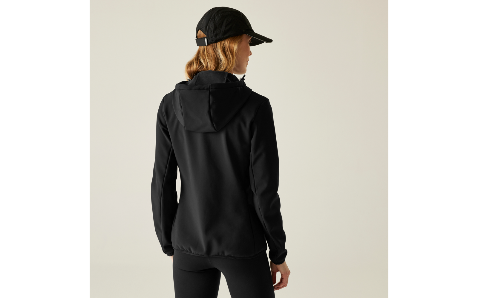 Frau von hinten mit schwarzer Cap, schwarzem Hoodie und schwarzer Hose vor hellem Hintergrund