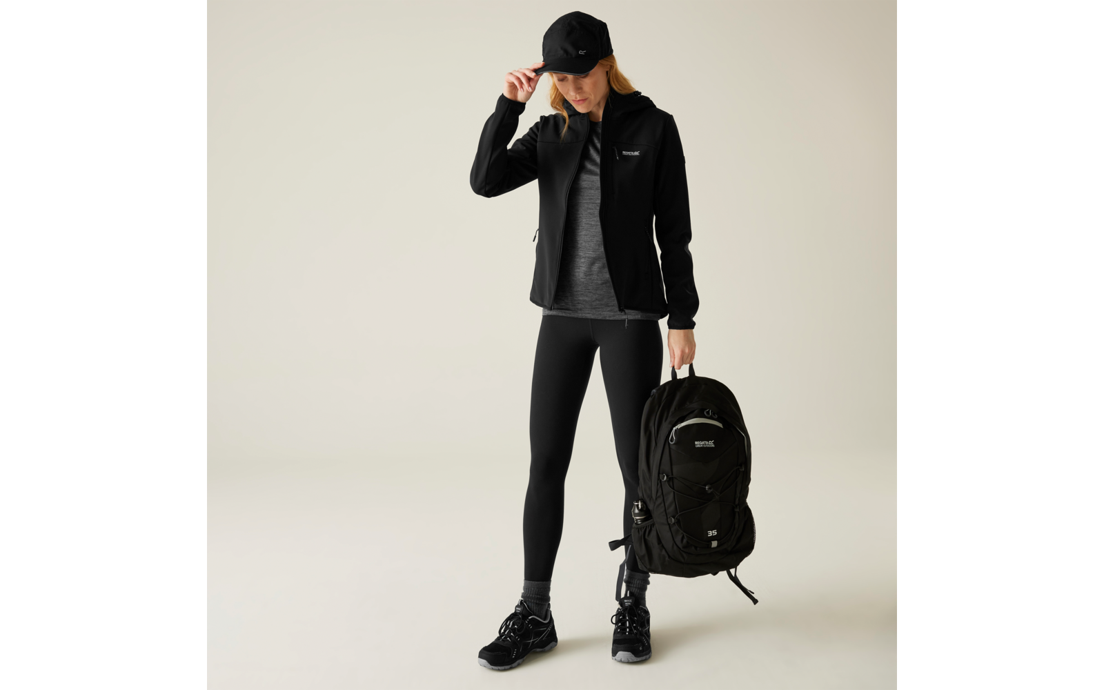 Person in schwarzer Sportkleidung hält schwarzen Rucksack in der Hand