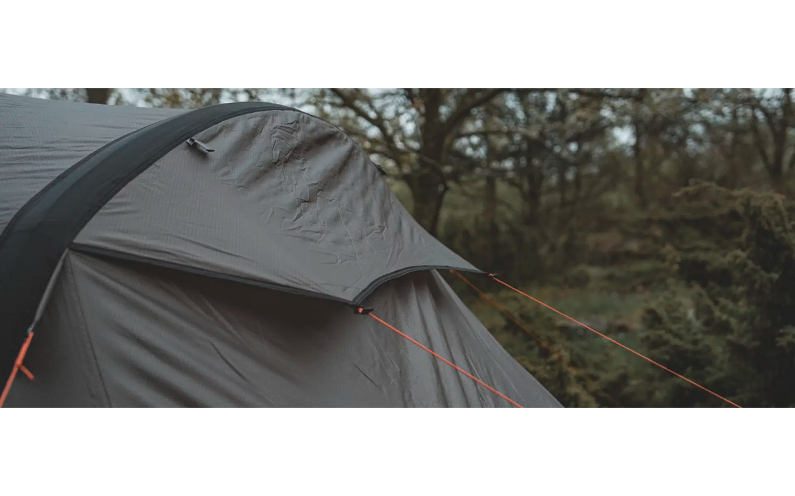 Ein graues Zelt steht auf einer Wiese mit Bäumen im Hintergrund