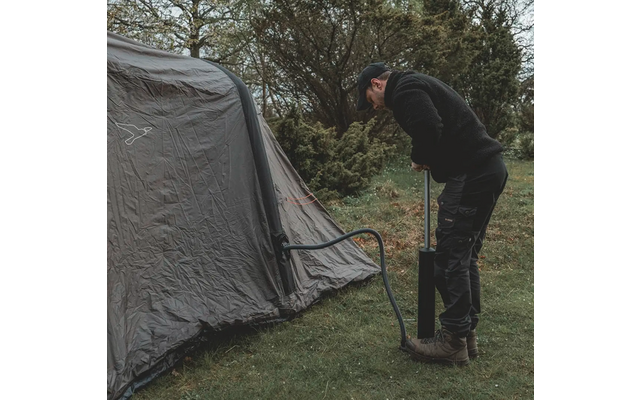 Person pumpt mit einer Luftpumpe ein graues Zelt auf, umgeben von Gras und Bäumen