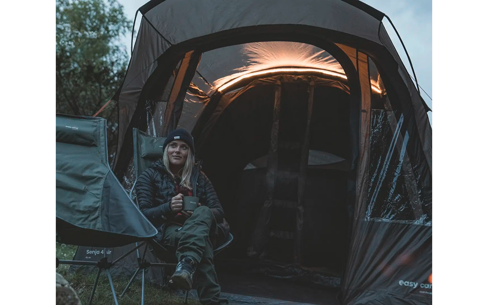 Person sitzt vor einem Zelt mit Beleuchtung im Inneren in einer Waldumgebung