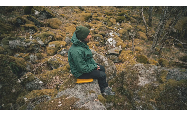 Person sitzt auf einem Felsen in bergiger Landschaft mit Kamera in der Hand
