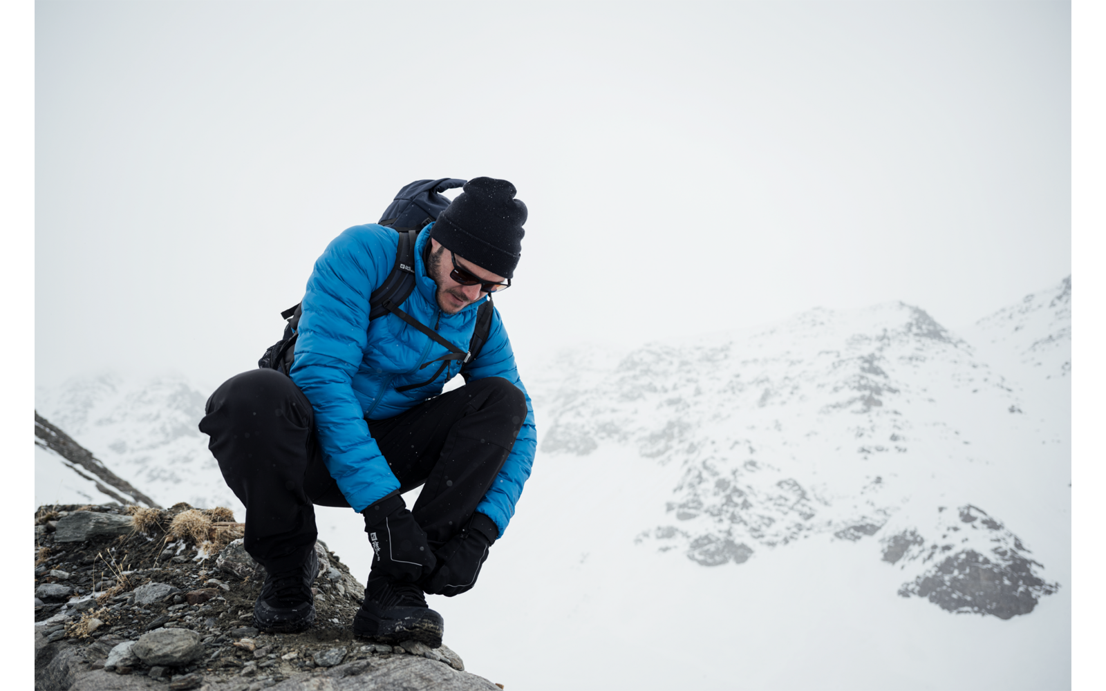 Man in blauwe jas met rugzak knielt op besneeuwde berg