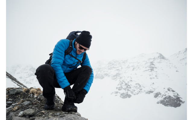 Man in blauwe jas met rugzak knielt op besneeuwde berg