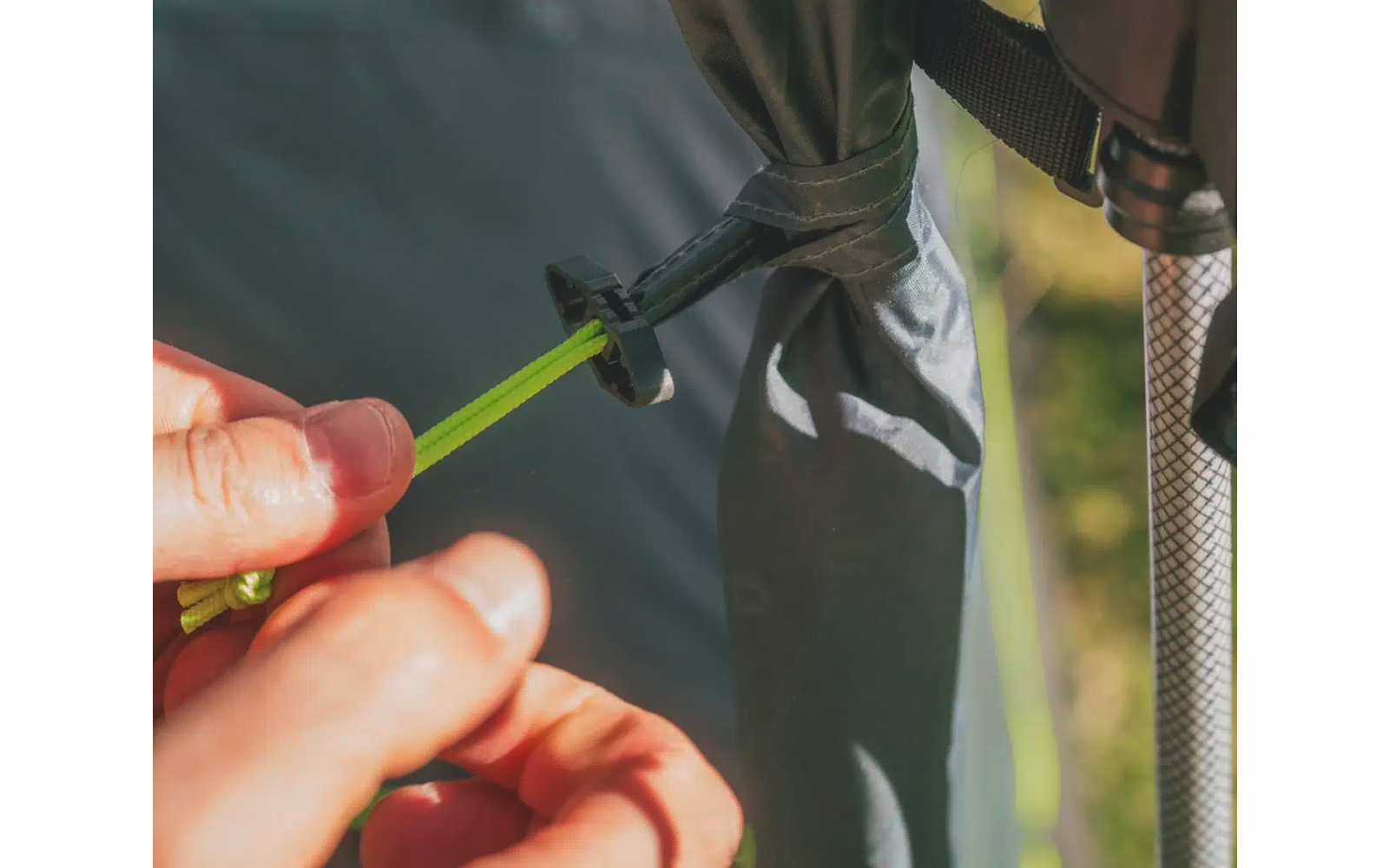 Hand schraubt grünes Seil an schwarzem Zelt fest