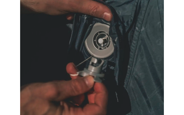 Hand hält ein rundes Metallobjekt mit einem Kabel an einer dunklen Stofffläche