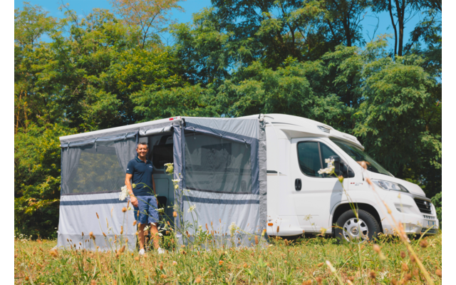 Uomo accanto a un camper con tenda da sole montata in un campo verde