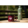 Roter Emaille-Campingbecher mit weißem "camp life"-Logo vorn auf einem Holztisch; unscharfe grüne Thermosflasche im Hintergrund