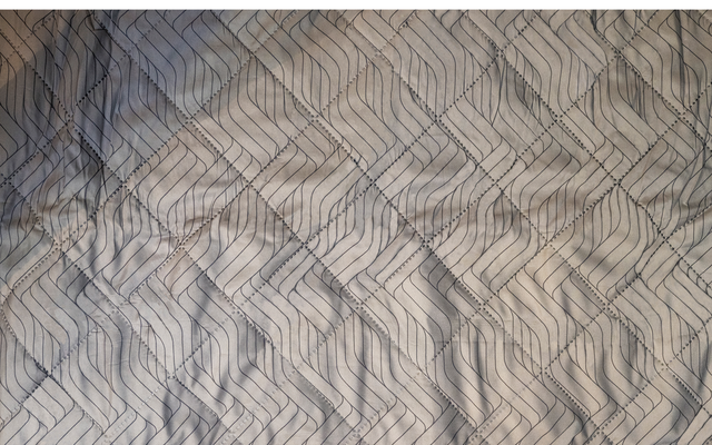 Bett mit hellgrauem Bezug und dunklem geometrischem Muster