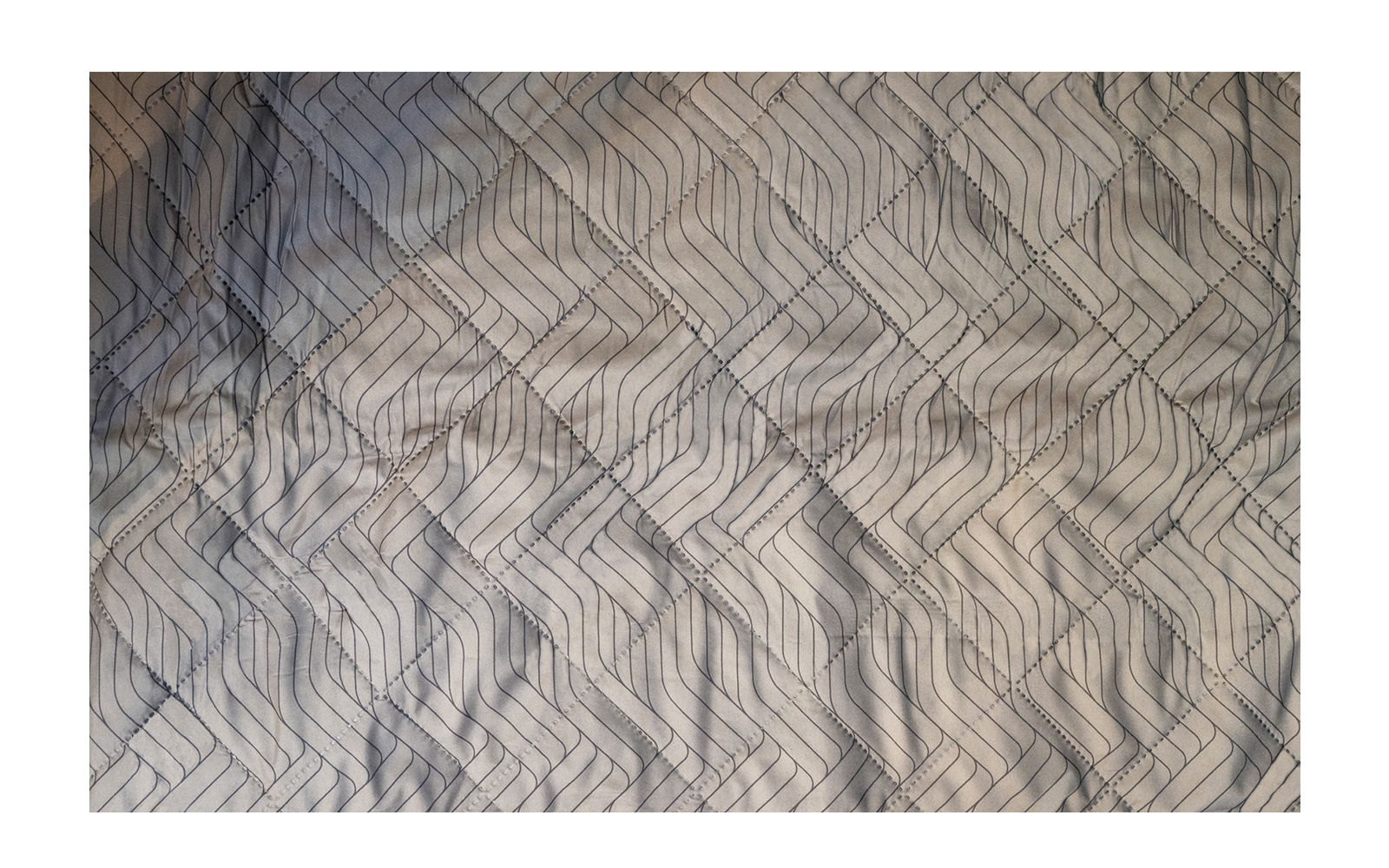 Bett mit hellgrauem Bezug und dunklem geometrischem Muster