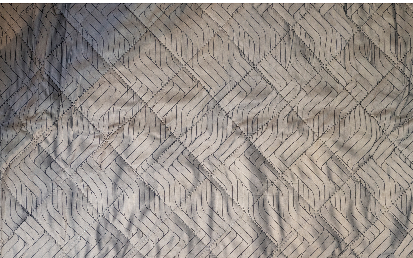 Bed with light gray cover and dark geometric pattern