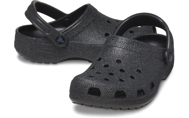 Dos zuecos negros con brillo, orificios de ventilación y tiras traseras ajustables, uno ligeramente delante del otro