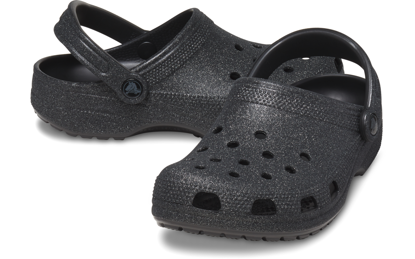 Dos zuecos negros con brillo, orificios de ventilación y tiras traseras ajustables, uno ligeramente delante del otro