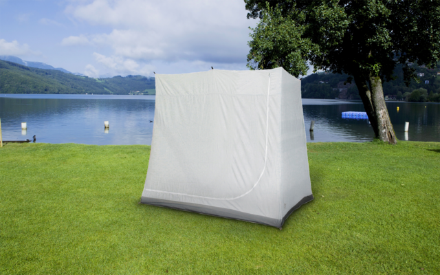 Zelt steht auf einer grünen Wiese vor einem See mit Bergen im Hintergrund