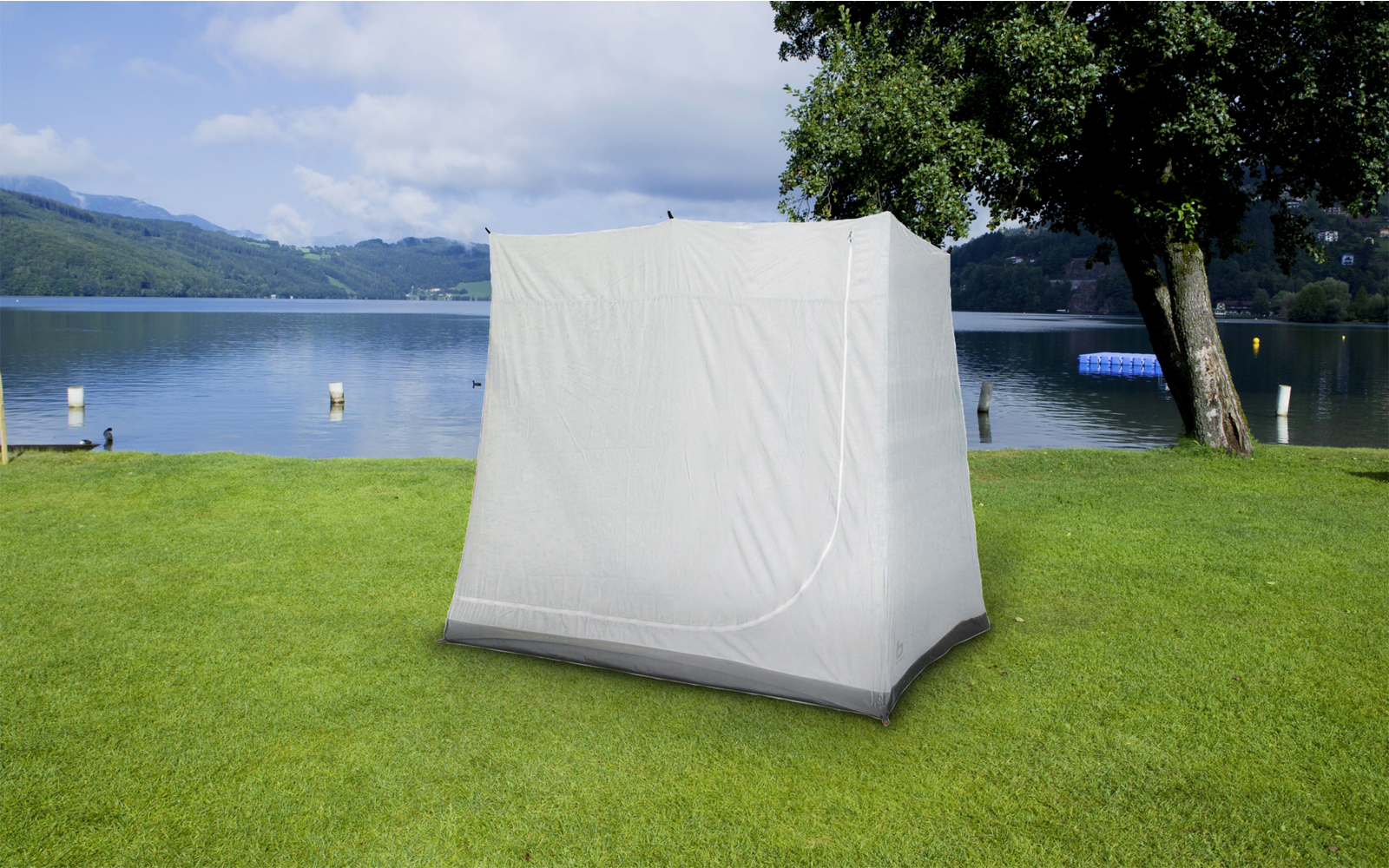 Zelt steht auf einer grünen Wiese vor einem See mit Bergen im Hintergrund